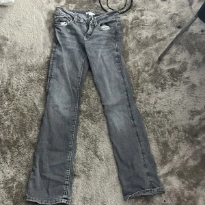 Grå bootcut jeans med fickdetaljer - Snygga grå jeans med bootcut passform och coola fickdetaljer bak med knappar. Jeansen har en klassisk femficksdesign och är tillverkade i ett mjukt denimtyg. De är 164cm långa.