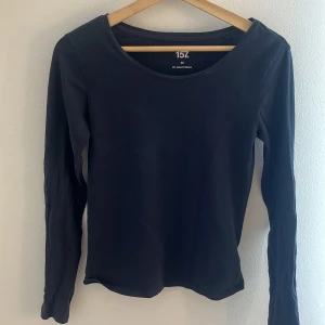 Svart långärmad tröja från 157 - En basic svart långärmad tröja från 157 i mjuk bomull med lite stretch. Enkel och stilren med rund halsringning, perfekt att matcha med jeans eller kjol. Materialet är 95% bomull och 5% elastan för en skön passform.