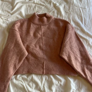 Rosa croppad stickad polotröja - Supermysig croppad polotröja i en dämpad rosa ton. Tröjan är stickad med bred ribbad mudd i hals och nederkant, samt har en markerad söm mitt fram och bak. Perfekt för lager-på-lager och chill höst- eller vinterstil.