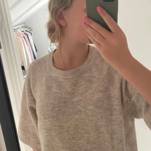 Beige stickad tröja från 157 - Mysig beige stickad tröja från 157 med rund halsringning och avslappnad passform. Tröjan har halvlånga ärmar och ribbade muddar vid hals och nederkant. Perfekt för lager-på-lager under höst och vinter.