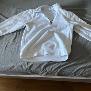 Vit half zip sweatshirt från Clique - Vit sweatshirt från Clique med halv dragkedja och hög krage. Tröjan är i mjuk bomull och har lång ärm och relaxed fit. Perfekt för chill dagar eller när du vill ha en clean och enkel look.