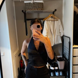 Svart omlott halterneck topp - Säljer en svart omlott halterneck topp med knyt i nacken och ryggen. Toppen är croppad och har öppen rygg, perfekt för dig som vill ha en stilren och trendig look. Snygg att matcha med både jeans och kostymbyxor.