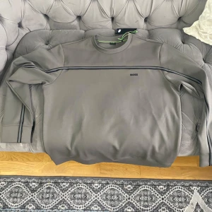 Grå sweatshirt från BOSS XXL - Snygg grå sweatshirt från BOSS i storlek XXL. Helt ny köpt present till min pappa men han vill inte ha den typisk envis arab pappa så säljer den för att få tillbaka lite pengar. Pris kan diskuteras 