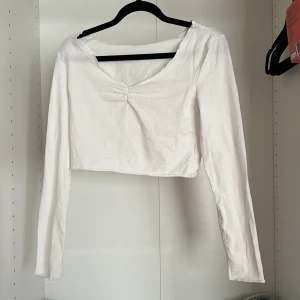 Vit croppad långärmad topp - Säljer en vit croppad topp med lång ärm och snygg v-ringning framtill. Perfekt att matcha med höga jeans eller kjol för en clean look.