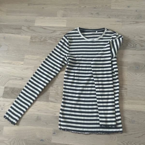 Randig långärmad tröja från Name It - Säljer en svart och vit randig långärmad tröja från Name It i ribbad bomull. Tröjan har smal passform och söta volangdetaljer vid ärmslut och nederkant. Perfekt för dig som gillar klassisk stil med en twist.