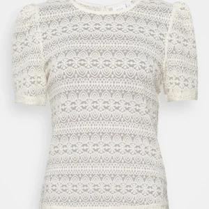 Vit spetsblus från Vila - Superfin vit blus från Vila med korta puffärmar och vackert spetsmönster över hela toppen. Blusen har rund halsringning och en liten knappdetalj i nacken. 