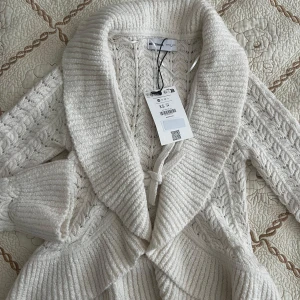 Vit stickad kofta från Bershka XS - Supermysig vit stickad kofta från Bershka i storlek XS. Koftan har grovstickat mönster, bred krage och knytband i midjan. Prislappkvar pris kan diskuteras 