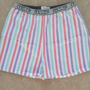Shorts - Färgglada shorts från Wow med vertikala ränder i lila, mintgrönt, rosa, rött och vitt. Resårlinningen är glittrig silver med svart Wow-logga runtom. Perfekta för sommarens chill dagar. Lätta och sköna med loose fit.