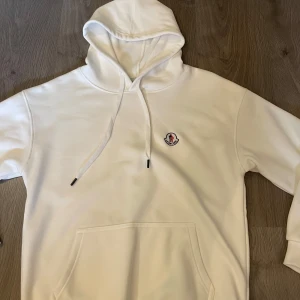 Moncler hoodie - Säljer en clean vit hoodie från Moncler med broderad logga på bröstet. Materialet känns mjukt och skönt. Storleken sitter som en M/S fast det står L.