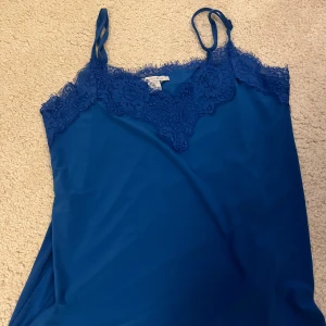Blå linnetopp med spets från newyorker  - Snygg blå linnetopp från newyorker med tunna axelband och v-ringad spetskant upptill. Toppen har en elegant och feminin look med fina spetsdetaljer längs halsringningen. Perfekt att styla med jeans eller kjol för en trendig vibe.