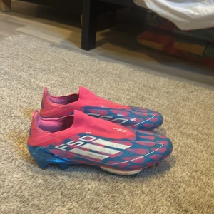 Adidas F50+ fotbollsskor blå/rosa - Säljer ett par Adidas F50+ fotbollsskor i en riktigt fet färgkombo av blått och rosa med vita detaljer. Skorna har en slimmad form, låg profil och mönstrad ovandel. Sulan är metallicblå med dobbar för gräsplan. Medföljer originalpåse och skohorn. Använda 2-3 gånger