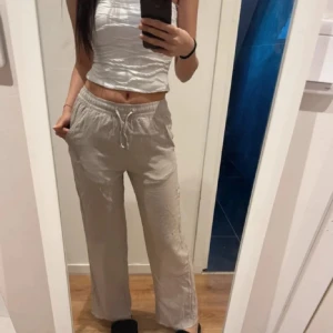 Beiga linnebyxor med snörning - Säljer ett par beiga linnebyxor med avslappnad passform och dragsko i midjan. Byxorna har raka, vida ben och är perfekta för en chill och luftig stil. Superbekväma och lätta att matcha med olika toppar.