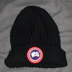 Svart ribbstickad mössa Canada Goose - Svart ribbstickad mössa från Canada Goose med klassisk uppvikt kant. Använd ca 3 gånger som ny