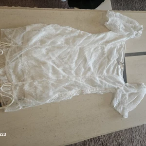 Vit spetsklänning från Divided H&M - Superfin vit kortklänning från Divided H&M med romantiska spetsdetaljer och puffiga kortärmar. Klänningen har en figurnära passform och är perfekt för sommarens alla tillfällen. Snygg omlottkänsla och transparent spets över hela plagget.