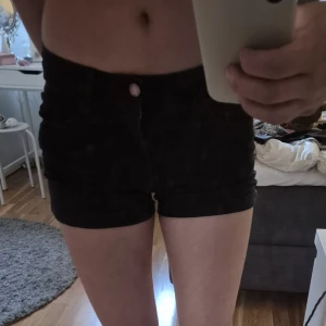 Svarta jeansshorts - Säljer ett par svarta, tighta jeansshort och klassisk femficksdesign. De har knapp och dragkedja framtill samt uppvikta benslut. Perfekta för varma dagar och en chill look.
