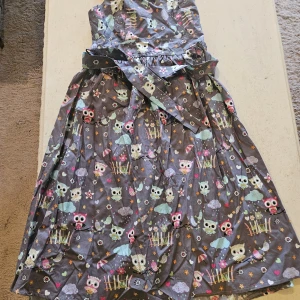 Grå ugglemönstrad klänning Bonny - Supersöt grå klänning från Bonny med färgglatt ugglemönster, hjärtan och blommor. Klänningen har axelband, omlottliv och knytband i midjan. Perfekt för dig som gillar lekfulla prints och vill sticka ut lite extra.