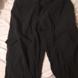 Svarta cargopants med fickor - Svarta cargopants med klassiska sidfickor och avslappnad passform. Perfekta för en chill och streetinspirerad look. Byxorna har en enkel design och är lätta att matcha med olika outfits.