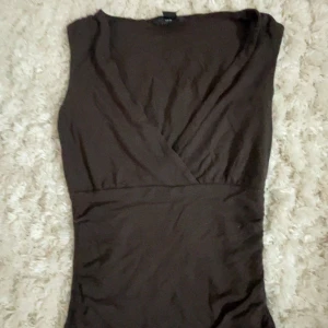 Brun omlottklänning från H&M XS - Snygg brun omlottklänning från H&M i storlek XS. Klänningen har ärmlös design och markerad midja som ger en smickrande siluett. Perfekt för dig som gillar stilrena och enkla plagg med en twist.