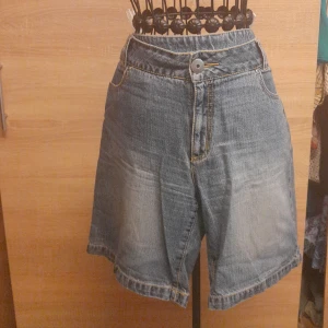 Blå jeansshorts från myWear - Snygga blå jeansshorts från myWear med klassisk femficksdesign och broderade detaljer på bakfickorna. De har normal passform, knapp och dragkedja framtill samt ljusare tvättade partier för en cool look. Perfekta för sommardagar och enkel att matcha med allt.