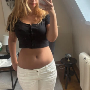 Svart croppad ribbad topp med knappar - Säljer en svart croppad topp med korta ärmar och snygg ribbad struktur. Toppen har knappar framtill och en djupare rundad ringning. 