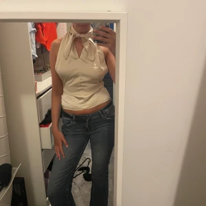 Champagnefärgad halterneck topp med knyt - Säljer en champagnefärgad halterneck topp i glansigt material. Toppen är ärmlös, croppad och har snygg knytning i nacken samt öppen rygg. Man kan knyta den lite som man själv känner då bandet där bak är väldigt långt 