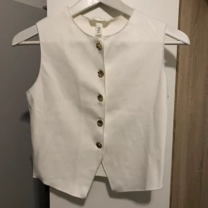 Vit väst med guldknappar från H&M - Stilren vit väst från H&M. Oanvänd med lappen på då jag blev sen med retur. Ord. pris 229. 