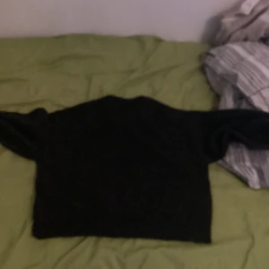 Svart stickad tröja med lång ärm - En svart stickad tröja med lång ärm, perfekt för kyliga dagar. Tröjan har en klassisk passform och är enkel att matcha med olika outfits. Mjuk och skön att bära, passar dig som gillar en stilren look.