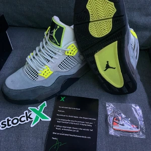 Nike Air Jordan 4 Retro Neon  - Nike Air Jordan 4 Retro Neon med grå mocka, svarta och neongula detaljer samt vit mesh. Snygg kontrast mellan olika grå nyanser och de neongula accenterna på snörning och sula. Ikonisk Jumpman-logga på plösen och Nike Air på hälen. Perfekta för dig som vill sticka ut.