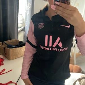 PSG långärmad fotbollströja Nike - Säljer en svart och rosa långärmad Paris Saint-Germain fotbollströja från Nike. Tröjan har rosa detaljer och logga på bröstet, samt tryck på både fram- och baksida. Ärmarna är ljusrosa med svarta inslag och tillverkad i ett lätt, sportigt material.