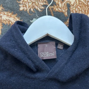 Mörkblå hoodie i kashmir från Oscar Jacobson - Snygg mörkblå hoodie från Oscar Jacobson i mjuk kashmir. Klassisk modell med huva och långa ärmar, perfekt för dig som gillar stilren och lyxig känsla. Tillverkad i Italien och passar dig som vill ha något både bekvämt och exklusivt. Föutom lite ludd är den i perfekt skick!