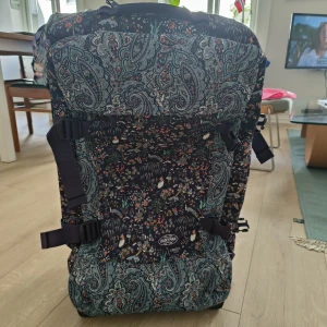 Mönstrad resväska Eastpak Liberty - Stor och rymlig resväska från Eastpak x Liberty med unikt paisley- och blommönster i mörkblått, turkos och inslag av orange. Väskan har hjul, utdragbart handtag och flera spännen för extra säkerhet. Perfekt för dig som vill sticka ut på resan. Är du i Oslo köp den idag! 