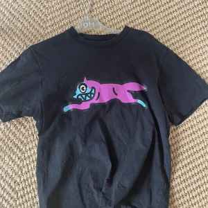 Svart Icecream t-shirt med kattmotiv - Svart t-shirt från Icecream by Billionaire Boys Club med en stor, färgglad kattgrafik i lila och blått på bröstet. Klassisk passform med rund hals och korta ärmar. Perfekt för dig som gillar streetwear och unika prints.