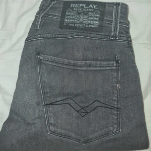 Replay Anbass grå slim jeans - (Pris Kan Diskuteras)       Snygga Replay Anbass jeans i grå tvätt med slim fit-passform. Klassisk femficksmodell med svarta sömmar på bakfickorna och Replay-logga. Jeansen är tillverkade i mjukt denimtyg och har dragkedjegylf samt bälteshällor.