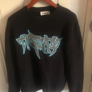 Svart stickad tröja från Weekday - Svart stickad tröja från Weekday med ett stort grafiskt tryck i grått och turkost framtill. Tröjan har rund halsringning och långa ärmar, perfekt för dig som gillar streetstyle och vill sticka ut lite extra.