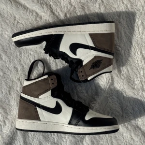 Nike Air Jordan 1 High svart/vit/brun - Nike Air Jordan 1 High med svart, vit och brun färgkombination. Klassisk high-top siluett med svart swoosh, snörning och perforerad tå. Ovandel i skinn och mocka för en lyxig känsla. Perfekta för dig som vill sticka ut med en ikonisk sneaker.  Dessa är helt nya och oanvända. Har tyvärr inte kvar lådan. 