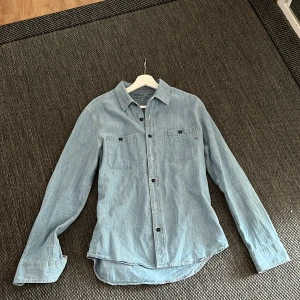 Ljusblå jeansskjorta från Replay - Säljer en snygg ljusblå jeansskjorta från Replay i storlek medium. Skjortan har två bröstfickor med knappar, klassisk krage och svarta knappar framtill. Perfekt för dig som gillar avslappnad stil och denim. Materialet är mjukt och bekvämt bomullstyg.