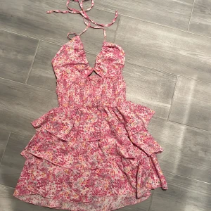 Rosa blommig volangklänning - Supersöt kort klänning med rosa och vita blommor, volanger i flera lager och smockad midja. Halterneck med knyt i nacken och lätt v-ringning framtill. Klänningen är från SHEIN! Storlek S