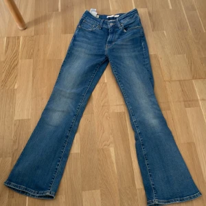 Levi's 725 High Rise Bootcut Jeans - Snygga Levi's Premium 725 High Rise Bootcut jeans i klassisk blå denim. Hög midja och bootcut-ben ger en retrovibe. Tillverkade i italiensk denim med fem fickor och coola slitningar. Perfekta för dig som gillar en tidlös och trendig look.