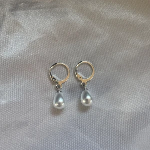 Pärlörhängen Silver - Säljer ett set med örhängen och halsband i silver- och guldfärg med droppformade vita pärlor. Örhängena har enkel klickstängning och halsbandet har grov kedja med flera pärldroppar. Perfekt för dig som gillar stilrena smycken med en twist. ❗️ Går att skickas med frimärke (ej spårbart) för endast 22kr. Kontakta mig då!❗️