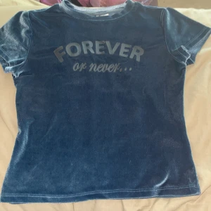 Blå sammetst-shirt från H&M Divided - Mörkblå t-shirt i mjuk sammet från H&M Divided med texten 'FOREVER or never...' framtill. Klassisk rund halsringning och korta ärmar. Skön och lite glansig känsla, perfekt för dig som gillar statement-plagg.
