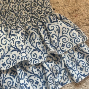 Blåvit volangkjol från Meet Tiger - Supersöt kort kjol från Meet Tiger i blått och vitt med snyggt mönster. Kjolen har bred smock i midjan och flera volanger som ger en flowy känsla. Perfekt för varma dagar och lätt att matcha med en enkel topp. Inbyggda shorts i kjolen. Storlek M/L men passar även S