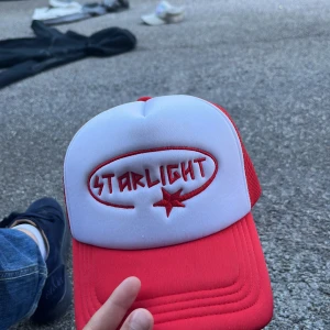 Röd och vit truckerkeps Starlight limited edition - Snygg truckerkeps i rött och vitt med broderad Starlight-logga och stjärna framtill. Kepsen har klassiskt nät på sidorna och justerbar snapback baktill. Perfekt för dig som vill sticka ut med en retro vibe.