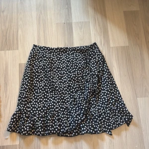 Svart blommig volangkjol  - Supersöt svart kortkjol från SHEIN med vita blommor och volangkant nertill. Kjolen har dragkedja i sidan och sitter snyggt i midjan. Perfekt för dig som gillar en feminin och trendig stil.