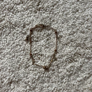 Guldfärgat armband med diamantdetaljer - Fint och nätt armband i guldfärgad metall med små kulor och glittrande stenar längs kedjan. Perfekt för dig som gillar diskreta men ändå snygga smycken. Liten karbinhake för enkel stängning. OBS!!! KOMMER GÖRAS RENT INNAN SICKAD