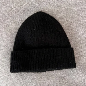 Svart stickad mössa - En klassisk svart stickad mössa med uppvikt kant. Perfekt för kyliga dagar och enkel att matcha med olika outfits. Mjuk och bekväm passform.