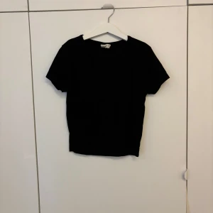 Svart t-shirt från Gina Tricot - En klassisk svart t-shirt från Gina Tricot i enkel design. T-shirten har rund halsringning och korta ärmar, perfekt för en stilren och basic look. Tillverkad i mjukt material som känns skönt mot huden.