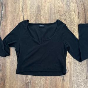 Svart croppad långärmad topp från Even & Odd - Svart croppad topp från Even & Odd med lång ärm och djup v-ringning. Enkel och stilren design som passar perfekt till jeans eller kjol.
