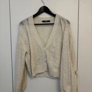 Vit stickad kofta från Bik Bok - Säljer en söt vit stickad kofta från Bik Bok i storlek S. Koftan har v-ringning, knappar framtill och ett fint hålmönster i materialet. Perfekt att slänga över en topp för en mysig look.