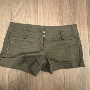Olivgröna shorts från Bershka - Snygga grön/gråa shorts från Bershka med dubbla knappar framtill. Klassisk femficksmodell med uppvikta benslut och dekorativa bakfickor. Dom tre första bilderna är lånade. Midje måttet är 39cm, storlek 36.  hör av sig om du har frågor eller funderingar 💕