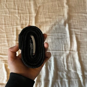 Svart flätat bälte med silverfärgat spänne - Säljer ett svart flätat bälte med ett stilrent silverfärgat spänne. Bältet har detaljer i svart skinn vid spännet och änden. Passar perfekt till jeans och ger en snygg touch till outfiten.